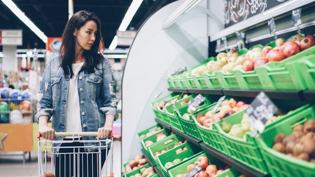 Shopper pushing a trolley through the fruit and vegetable aisle of a supermarket